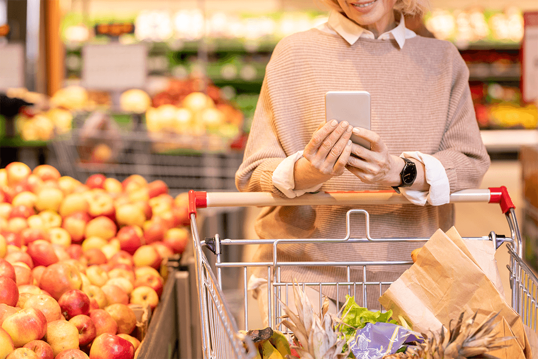 Mulher fazendo compras em supermercado com o celular nas mãos